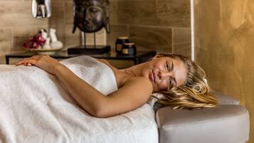 A person lying on a massage table in a room with a stone wall and a statue.