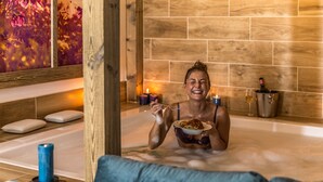 A person in a bathtub with a bowl of food, candles, and a bottle of wine on the side. - DAS AUNHAMER Suite & Spa Hotel - Adults Only (Bad Griesbach im Rottal)
