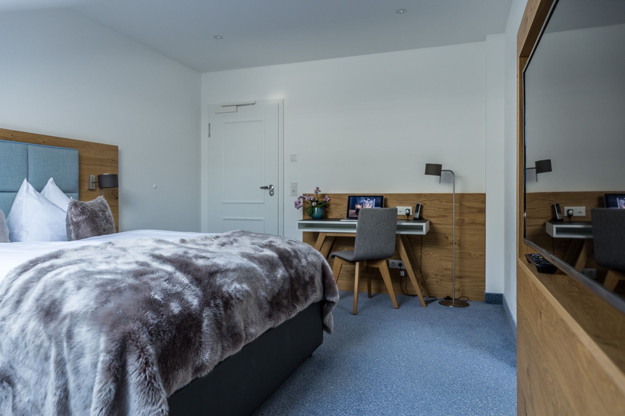 Una habitación de hotel con una cama, un escritorio, una silla, una computadora y un espejo grande.
