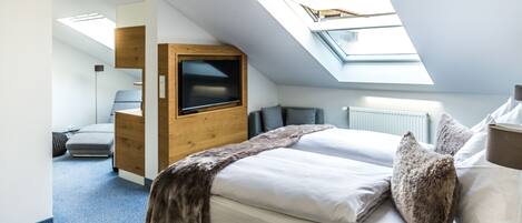Un dormitorio moderno con tragaluz, cama con ropa de cama blanca, armario de madera y escritorio con silla.