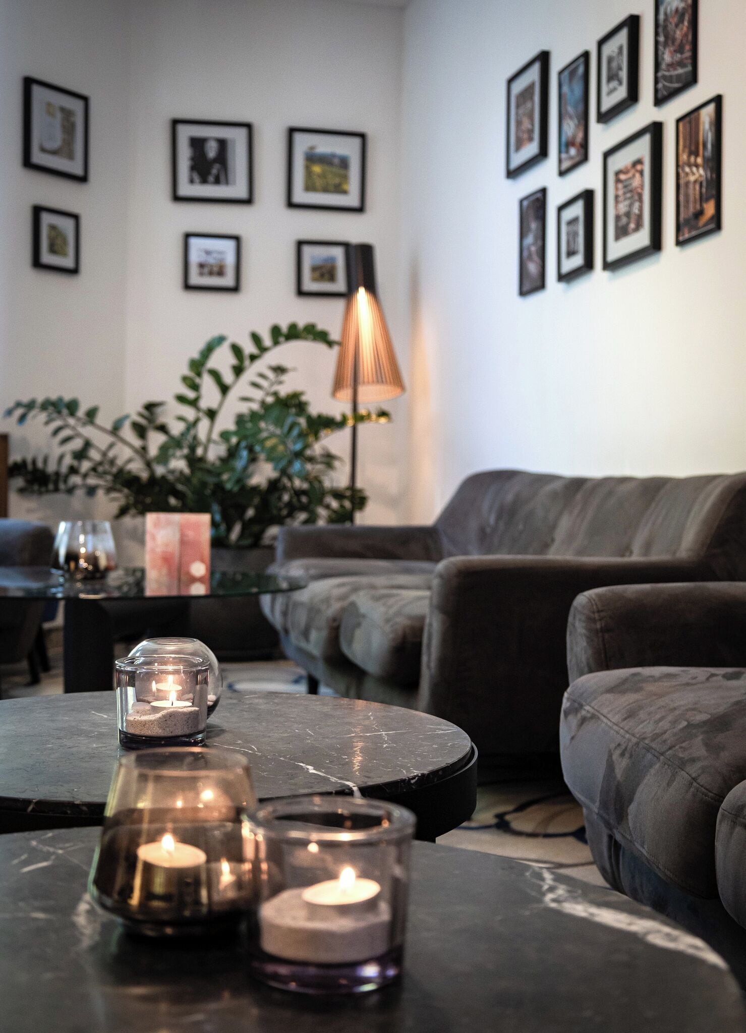 A living room with a sofa, a coffee table with candles, framed pictures on the wall, and a floor lamp.