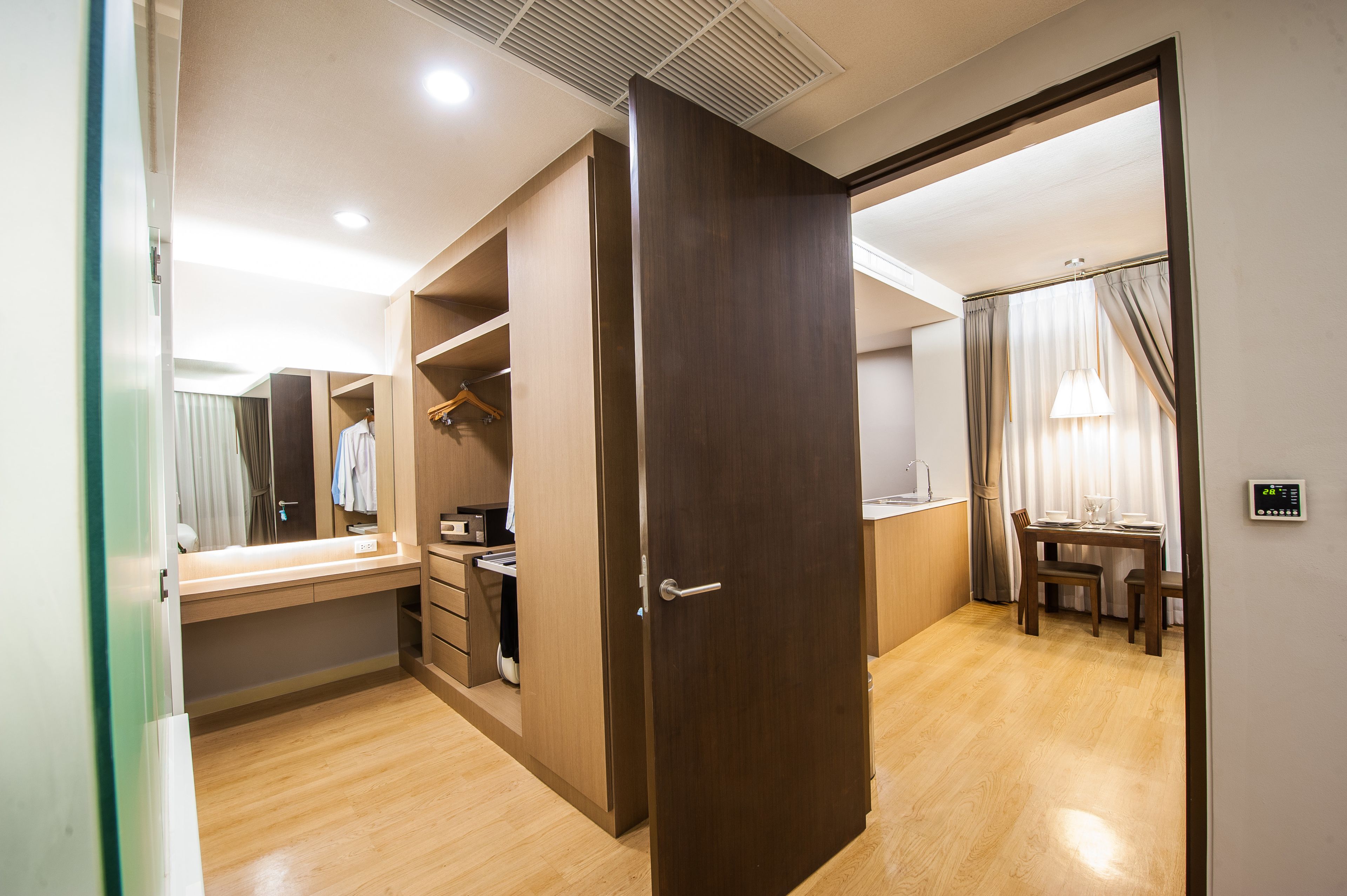 Habitación de hotel con piso de madera, un escritorio con silla, armario y zona de comedor con mesa y sillas.