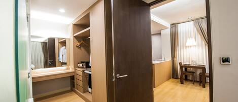 Habitación de hotel con piso de madera, un escritorio con silla, armario y zona de comedor con mesa y sillas.