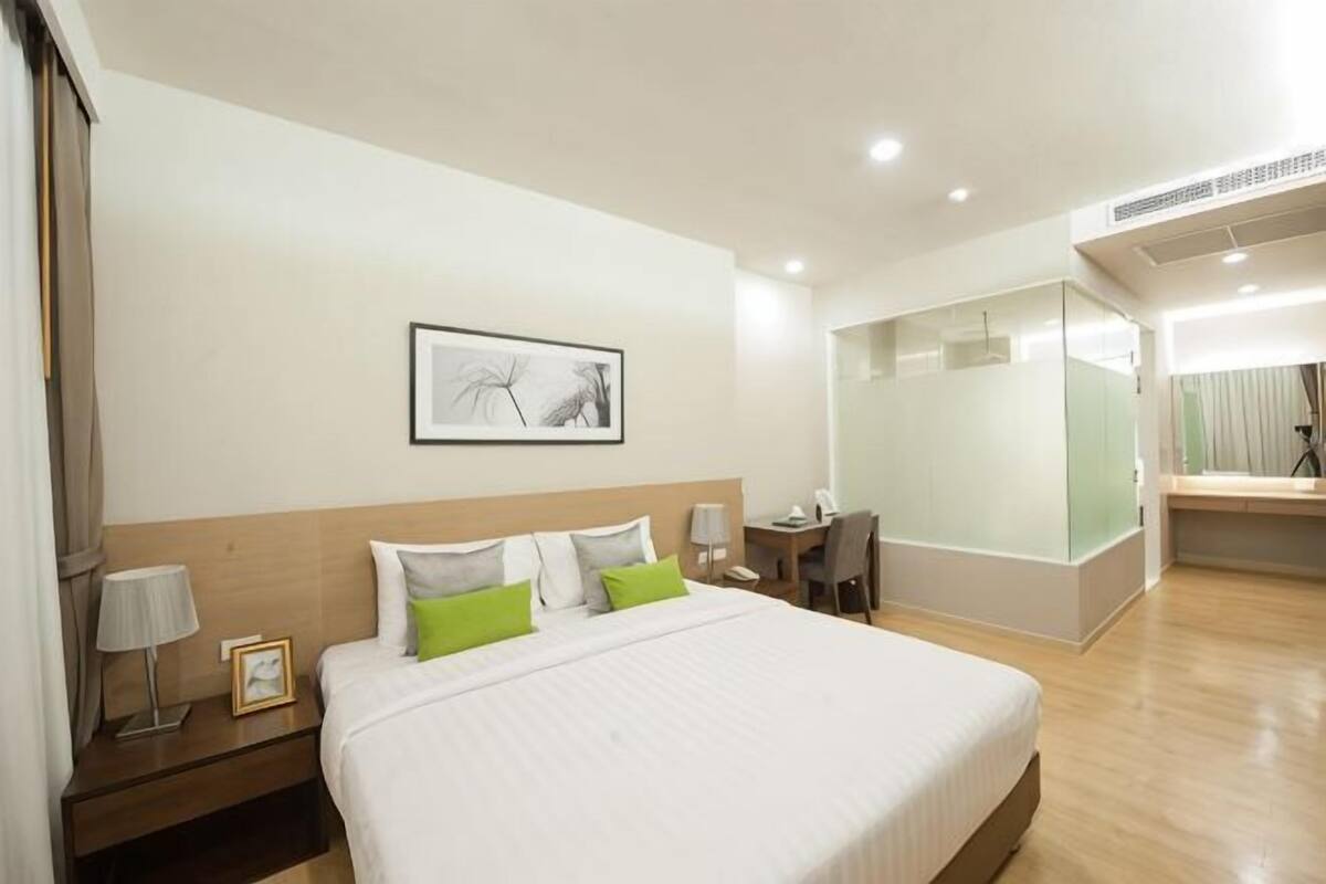 A hotel room with a large bed, bedside tables, a desk, a chair, a mirror, and a framed picture on the wall.