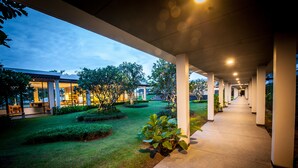 A covered walkway with a view of a building and landscaped garden. - Burgundy Residence (Si Maha Phot)