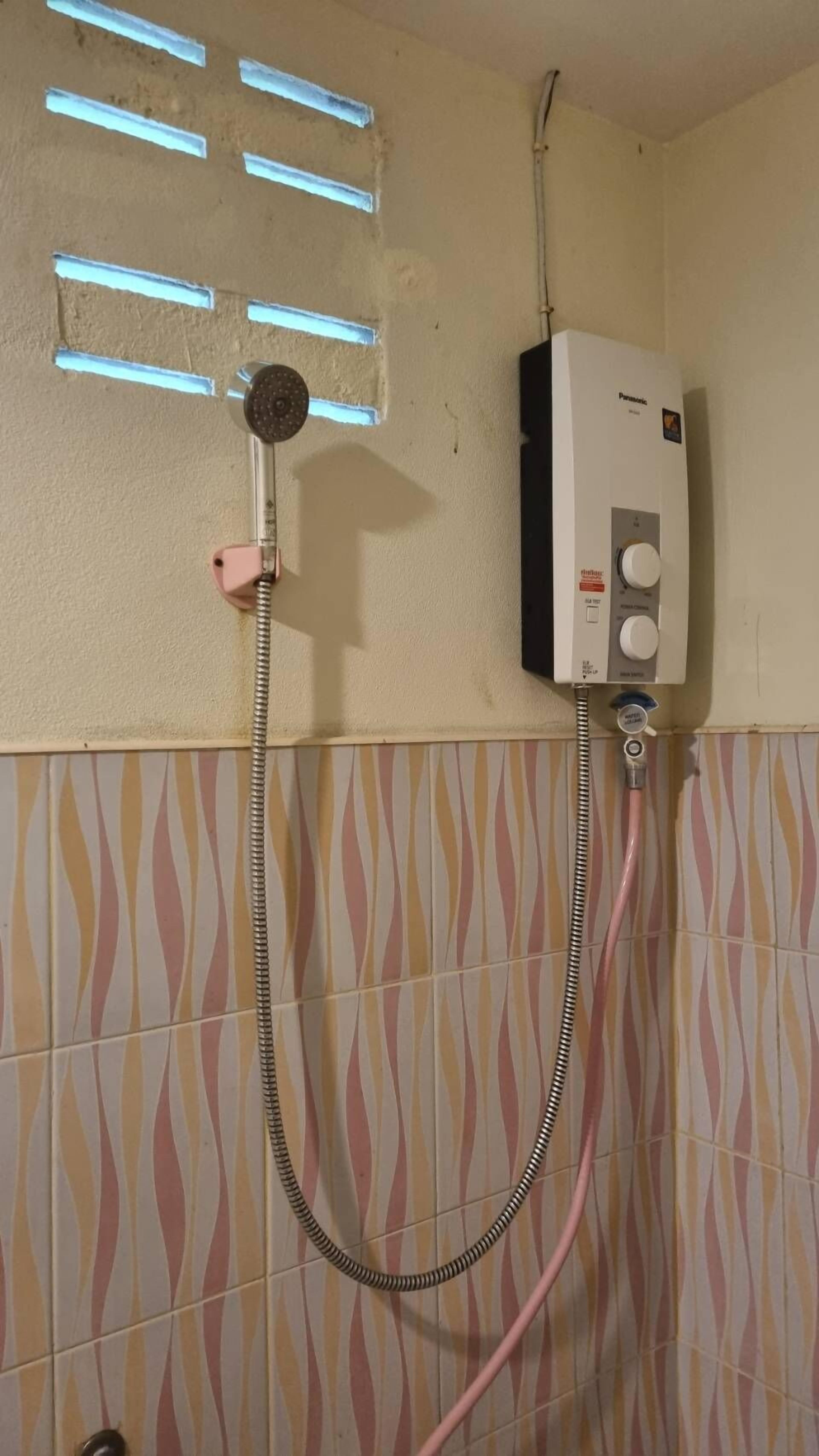 Un baño con ducha, un calentador en la pared y azulejos estampados.
