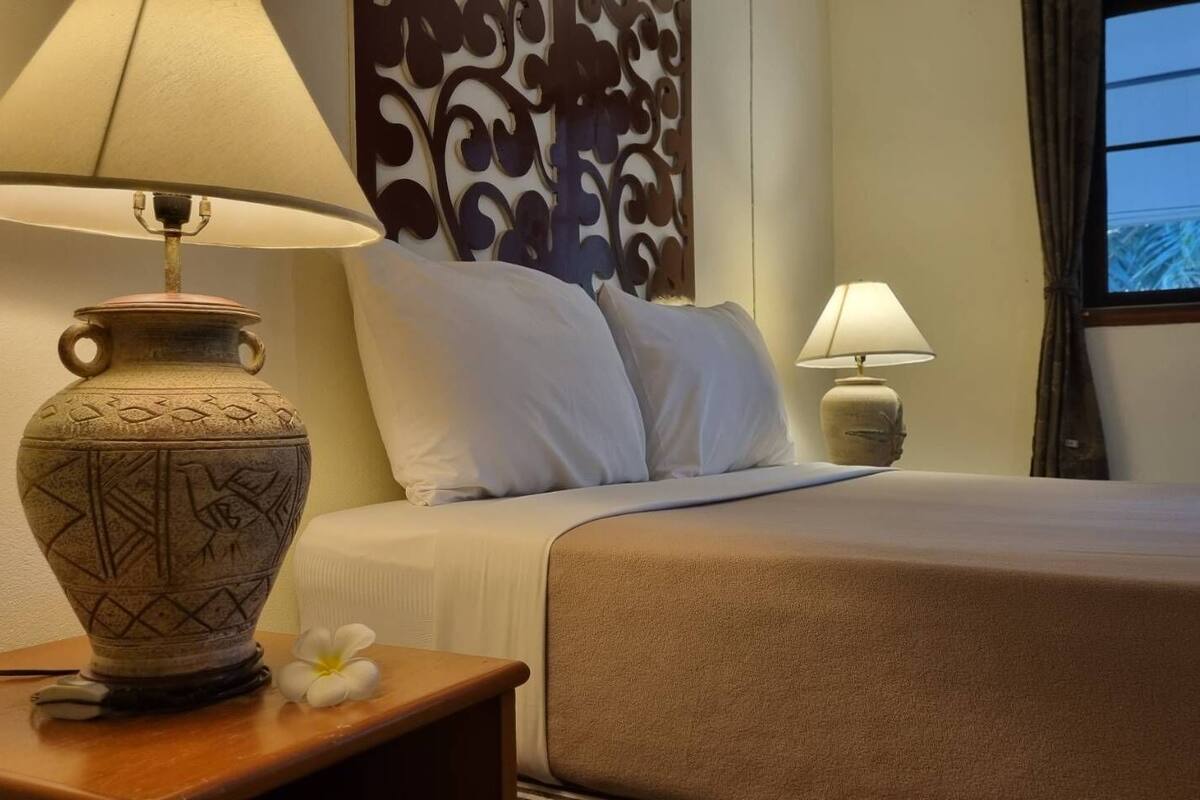 A hotel room with a bed, a nightstand with a lamp, and a decorative wall panel.