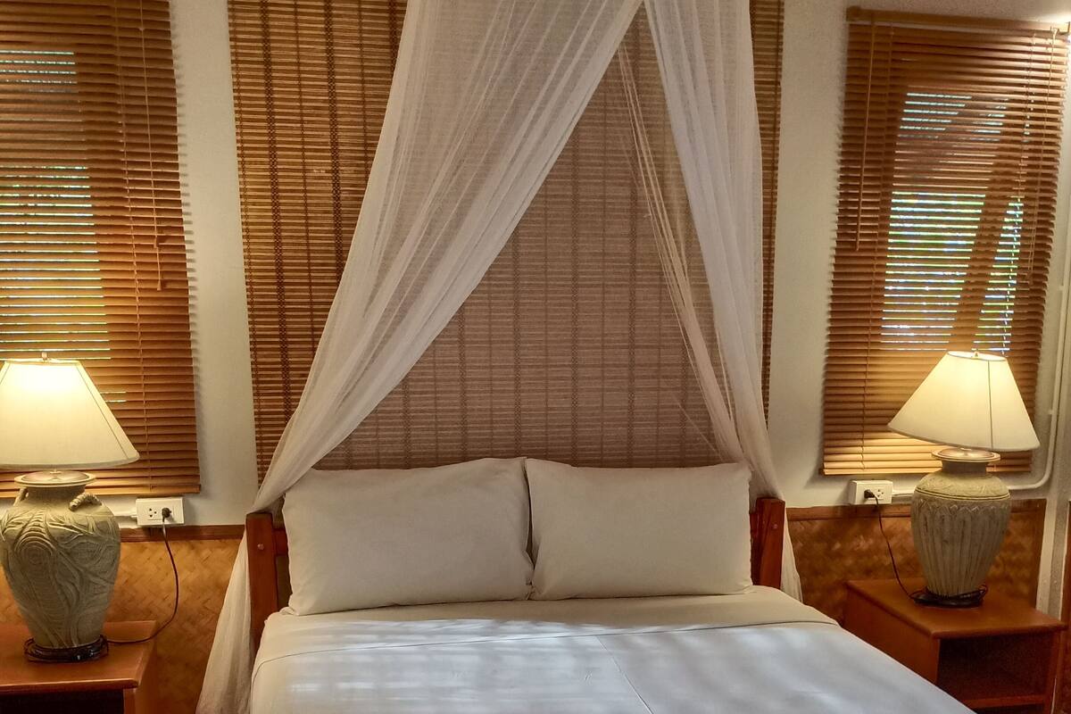 A neatly made bed with a canopy, two bedside lamps, and a wooden nightstand.