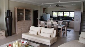 A modern living room with a sofa, dining table, and kitchen area. - The Beach Front Villas - North Bali (Sawan)