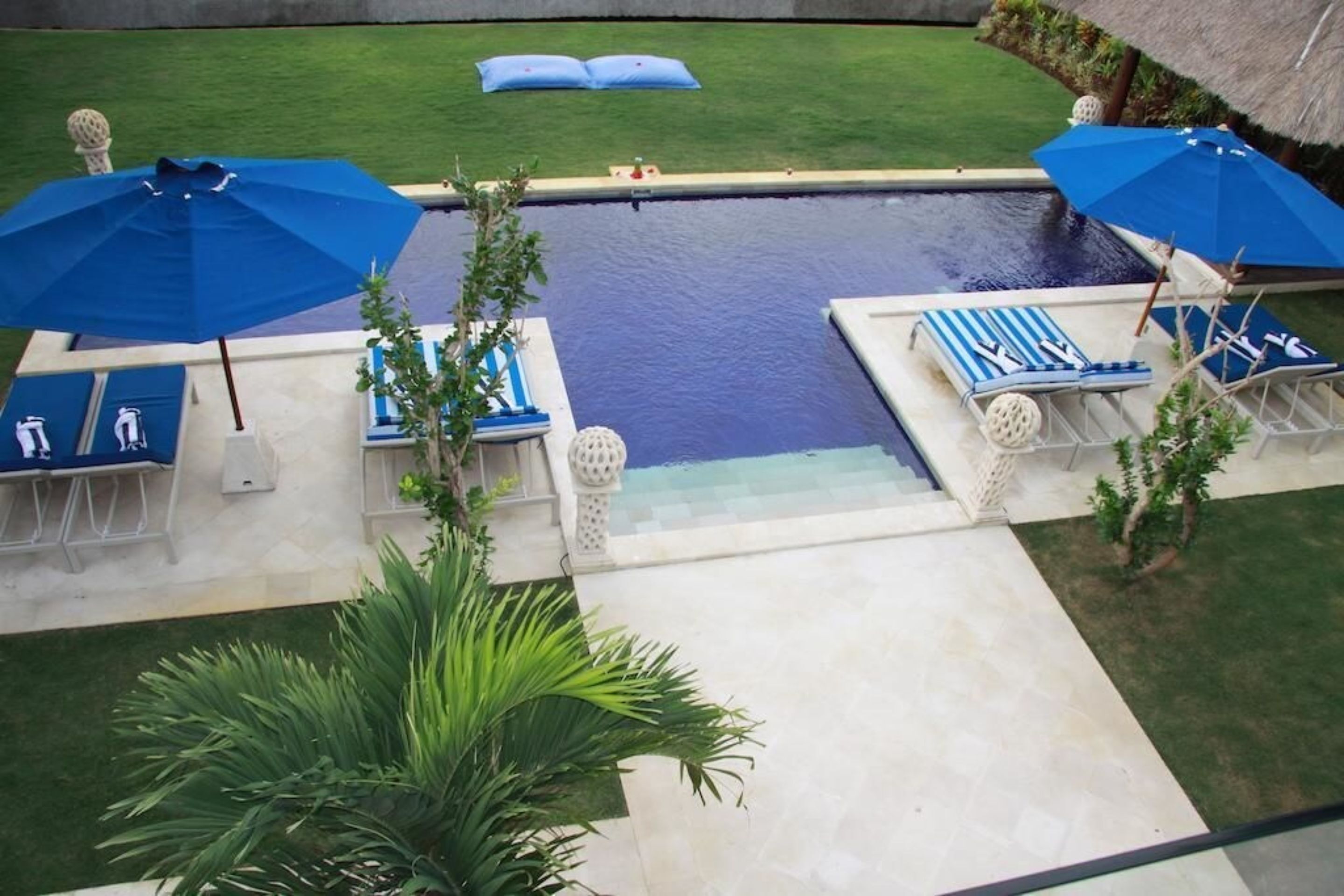 A swimming pool area with lounge chairs and umbrellas, surrounded by a well-maintained lawn and a small garden.