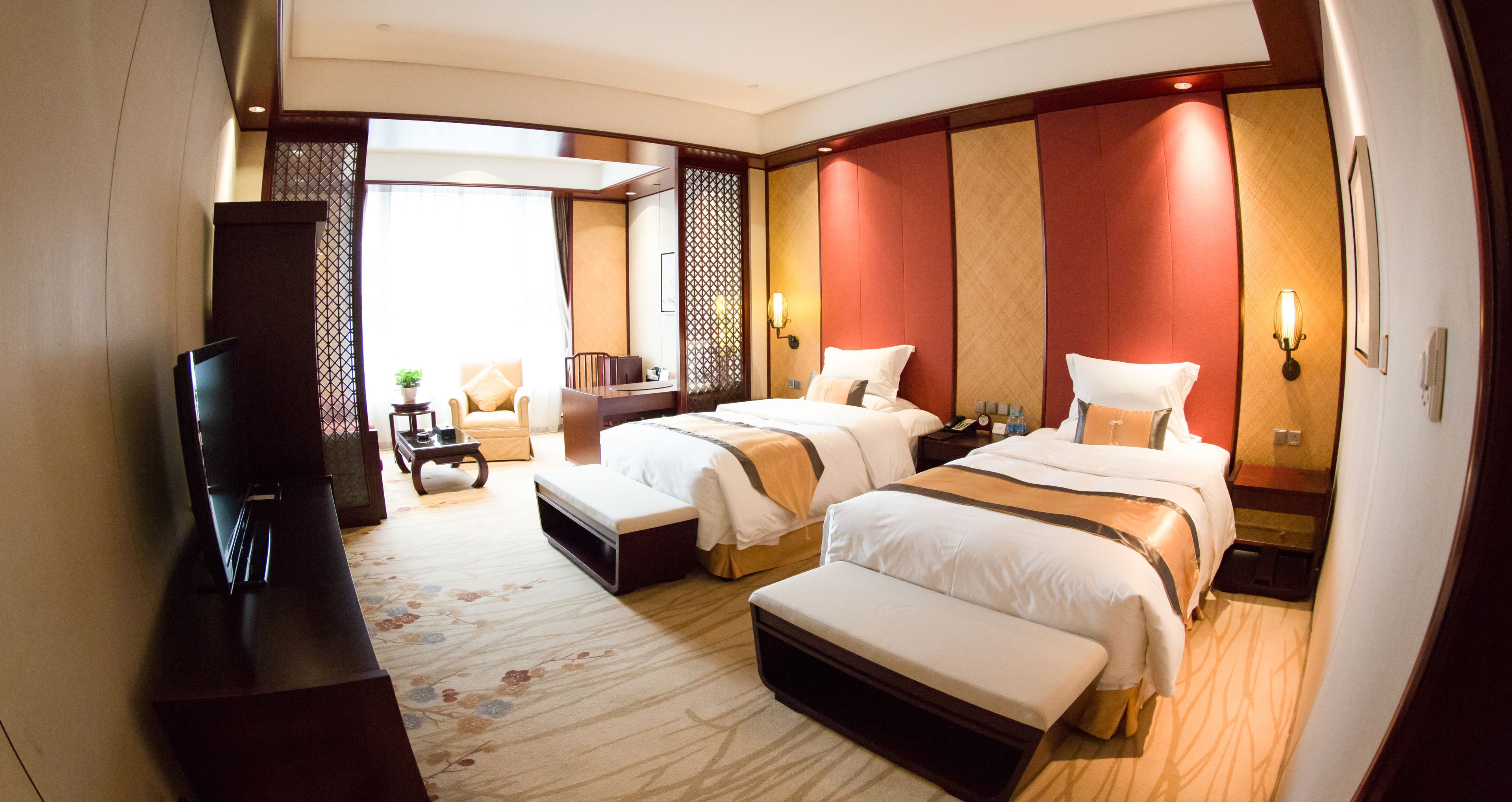 A hotel room with two beds, a TV, a desk, and a seating area.