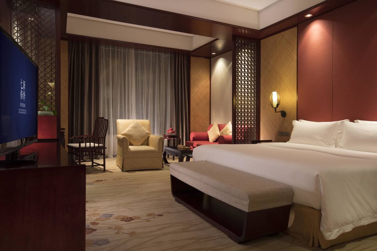 A hotel room with a large bed, a desk with a chair, a sofa, and a TV.
