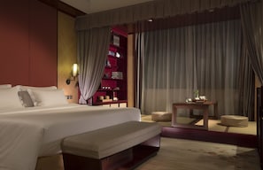 A hotel room with a large bed, a bedside table, a small seating area, and a built-in bookshelf. - Ovation Seven-Cultivation Hotel (Langfang)