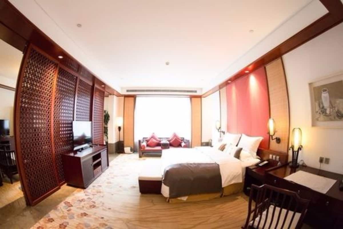 A hotel room with a bed, a desk, a TV, and a decorative screen.