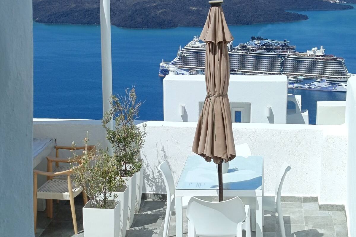 A terrace with a table and chairs, an umbrella, and a view of the sea and islands.