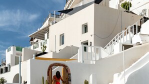 A white-washed building with a staircase leading to a wooden door. - Akron Cliff Suite (Santorini)