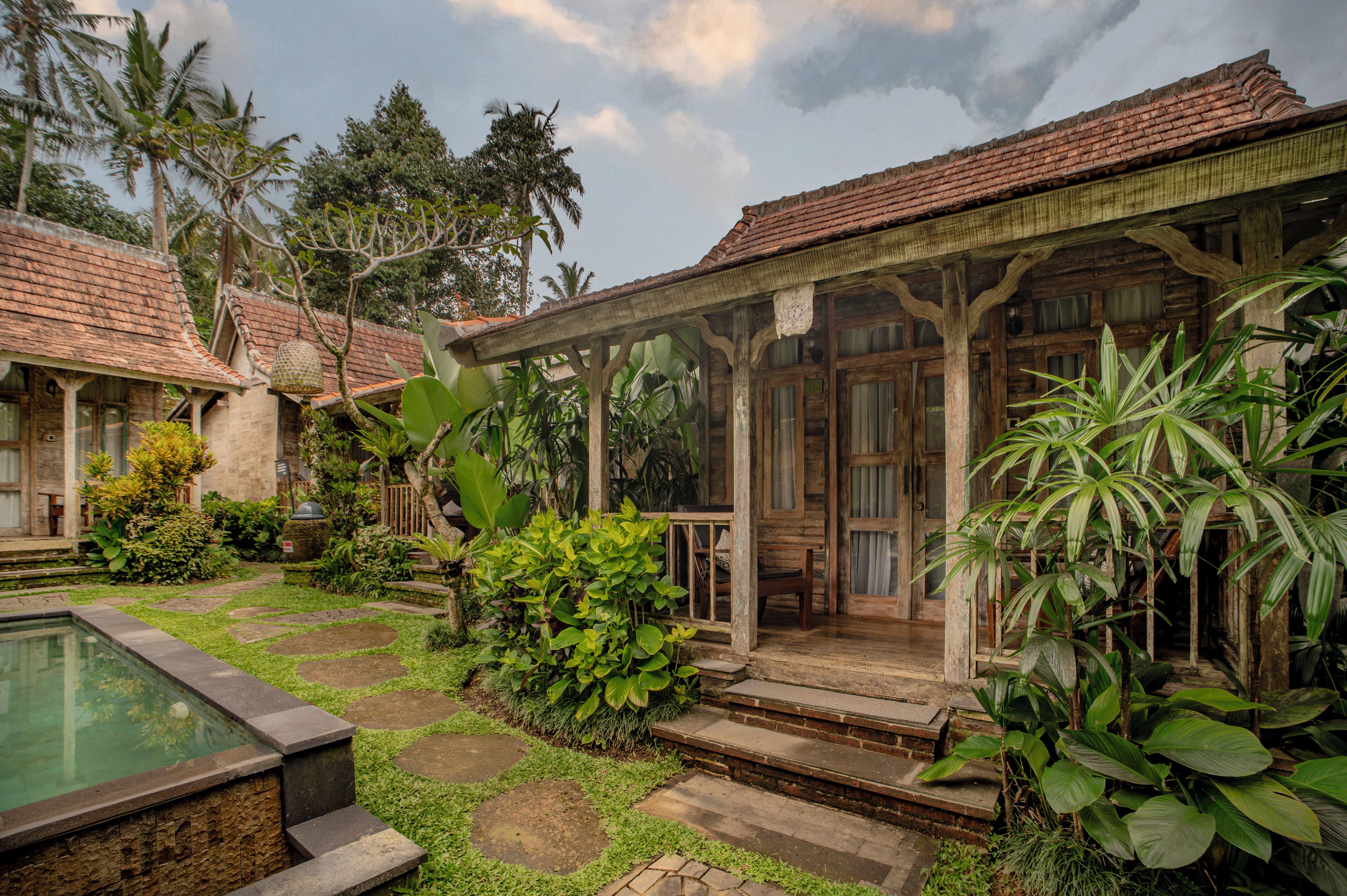 Uma casa de madeira tradicional com varanda coberta, piscina e vegetação tropical exuberante.