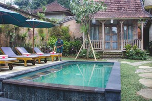 A swimming pool with lounge chairs and umbrellas, surrounded by greenery and a traditional house. - De Umah Bali Eco Tradi Home (Tembuku)