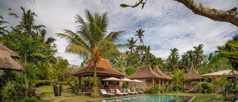 A pool area with lounge chairs, a thatched-roof structure, and tropical vegetation.