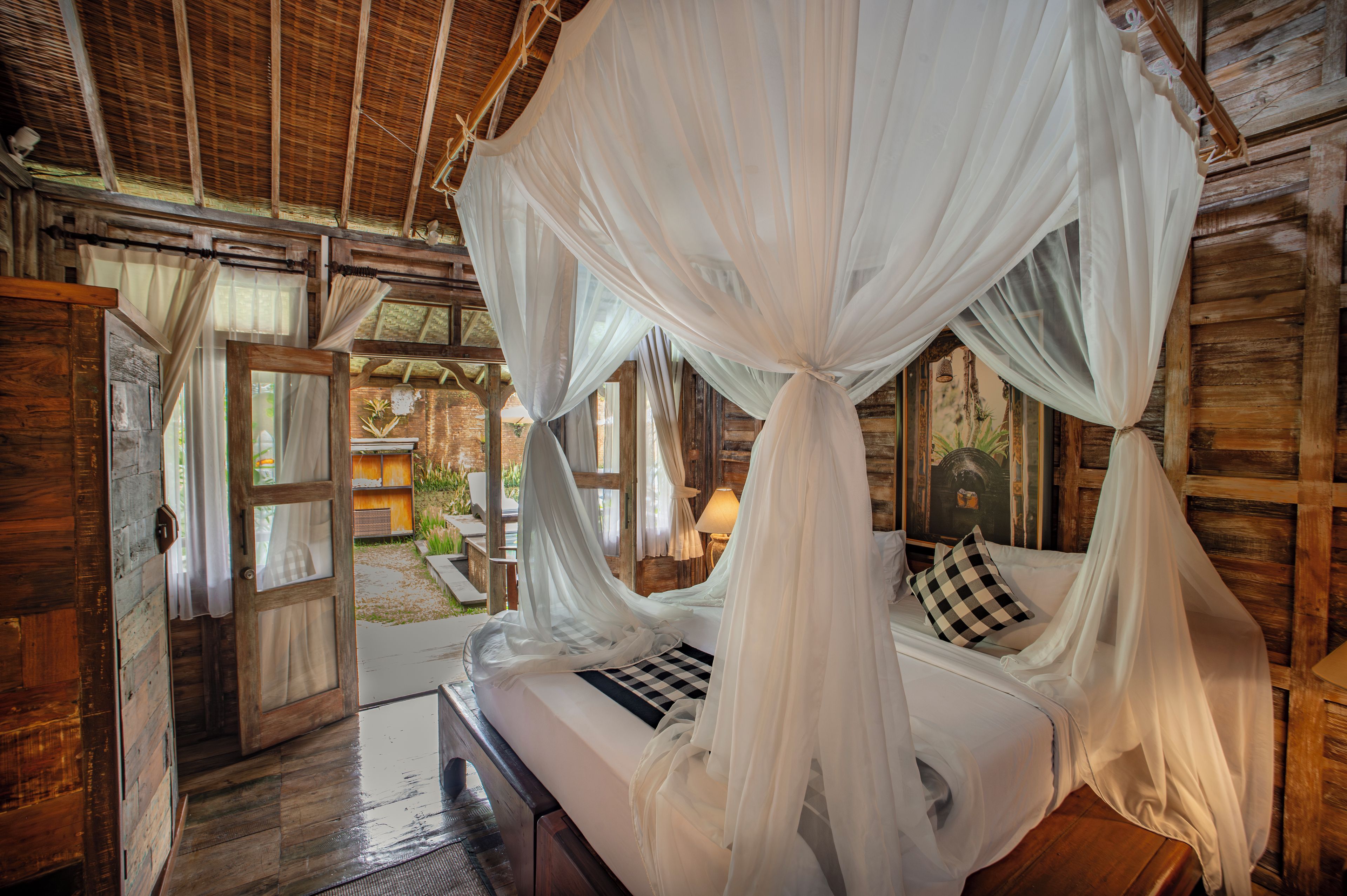 A wooden room with a bed under a canopy, a door leading outside, and a rustic interior.