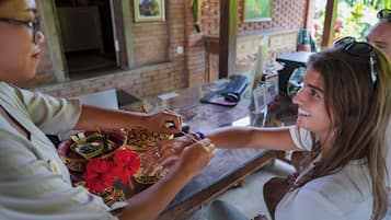 A person performing a ritualistic hand gesture, possibly a blessing or greeting, with a bowl of offerings and a small vase.