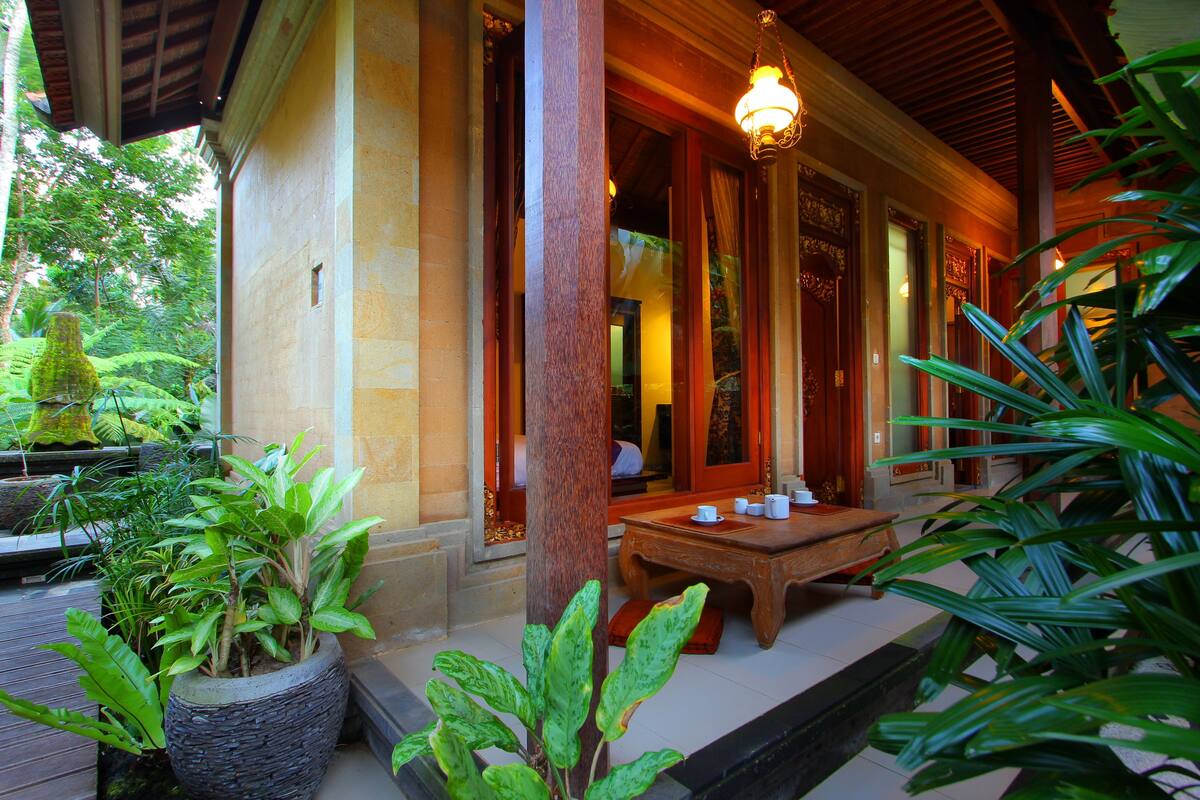 Un bâtiment traditionnel en bois, doté d’un porche couvert, de plantes en pot et d’une table avec des tasses et des soucoupes.
