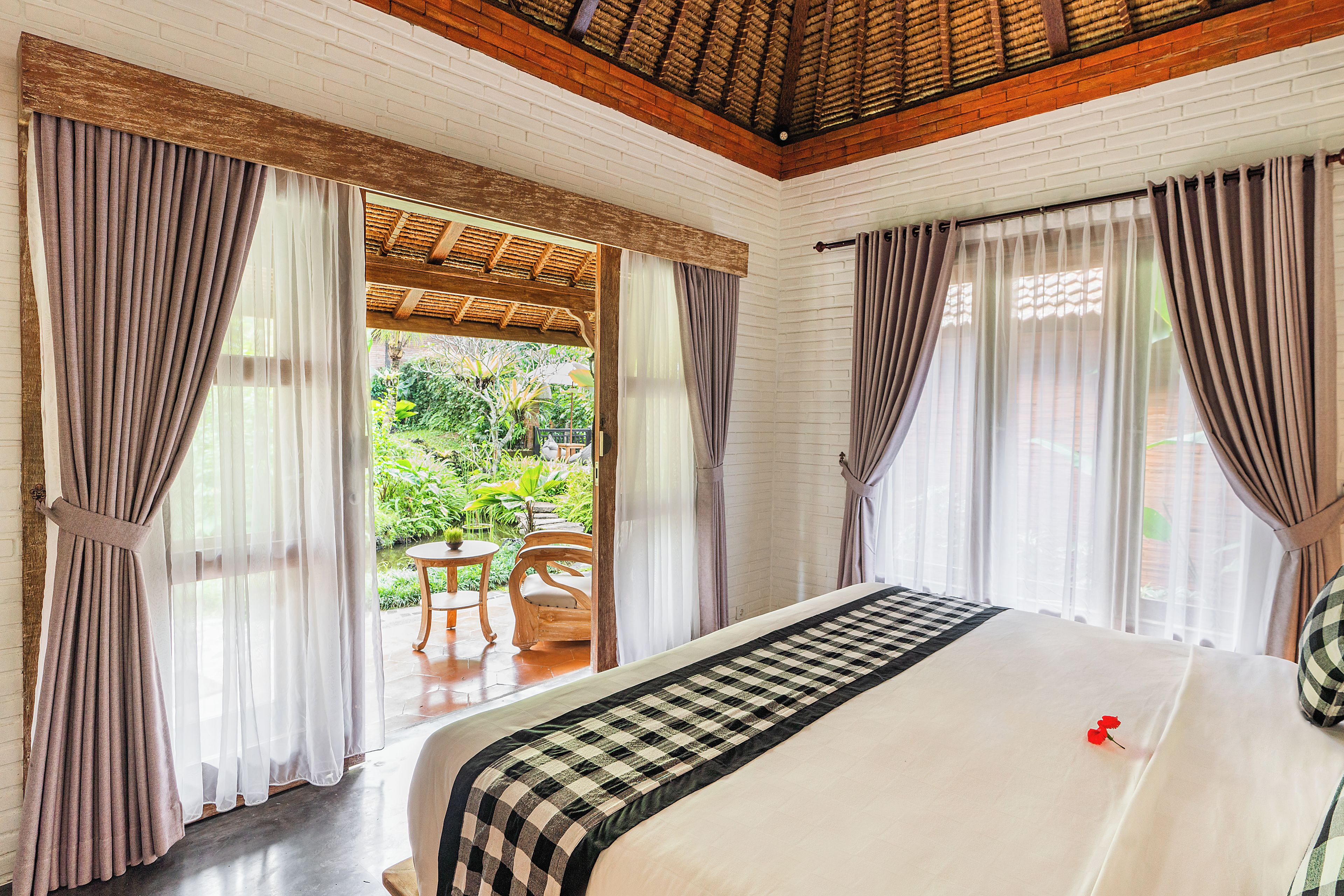 Une chambre d’hôtel avec un lit, des rideaux, une vue sur le jardin et un plafond en bois.