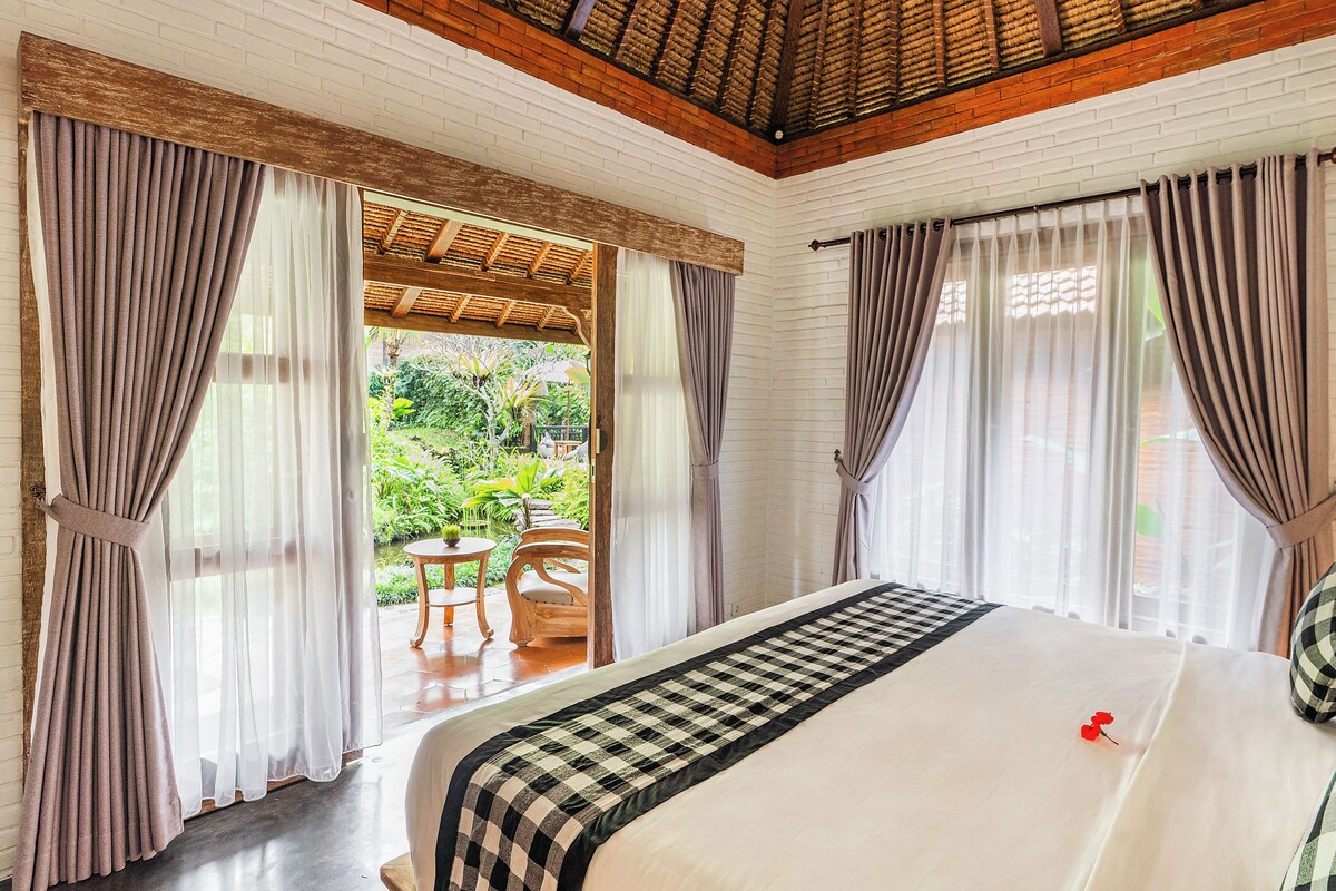 Une chambre d’hôtel avec un lit, des rideaux, une vue sur le jardin et un plafond en bois.