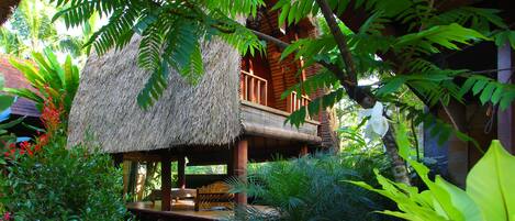 Una casa con tetto di paglia e un balcone in legno, immersa nel verde e decorata con piante in vaso.