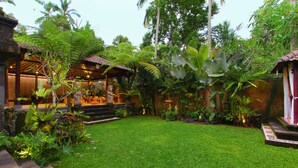 Un jardí exuberant amb un pràt perfectament cuidat, una construcció de fusta tradicional i diverses plantes tropicals.