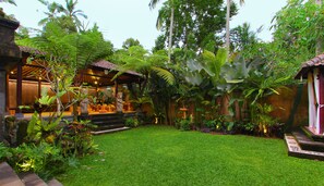 Un jardin luxuriant avec une pelouse bien entretenue, une structure traditionnelle en bois et diverses plantes tropicales.
