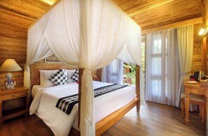 A wooden room with a four-poster bed, a nightstand, a lamp, and a view of greenery outside. - De Umah Bali Eco Tradi Home (Tembuku)