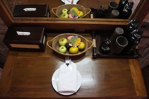 Una mesa de madera con un plato, un servilleta doblada, una cesta de frutas y una botella de agua.