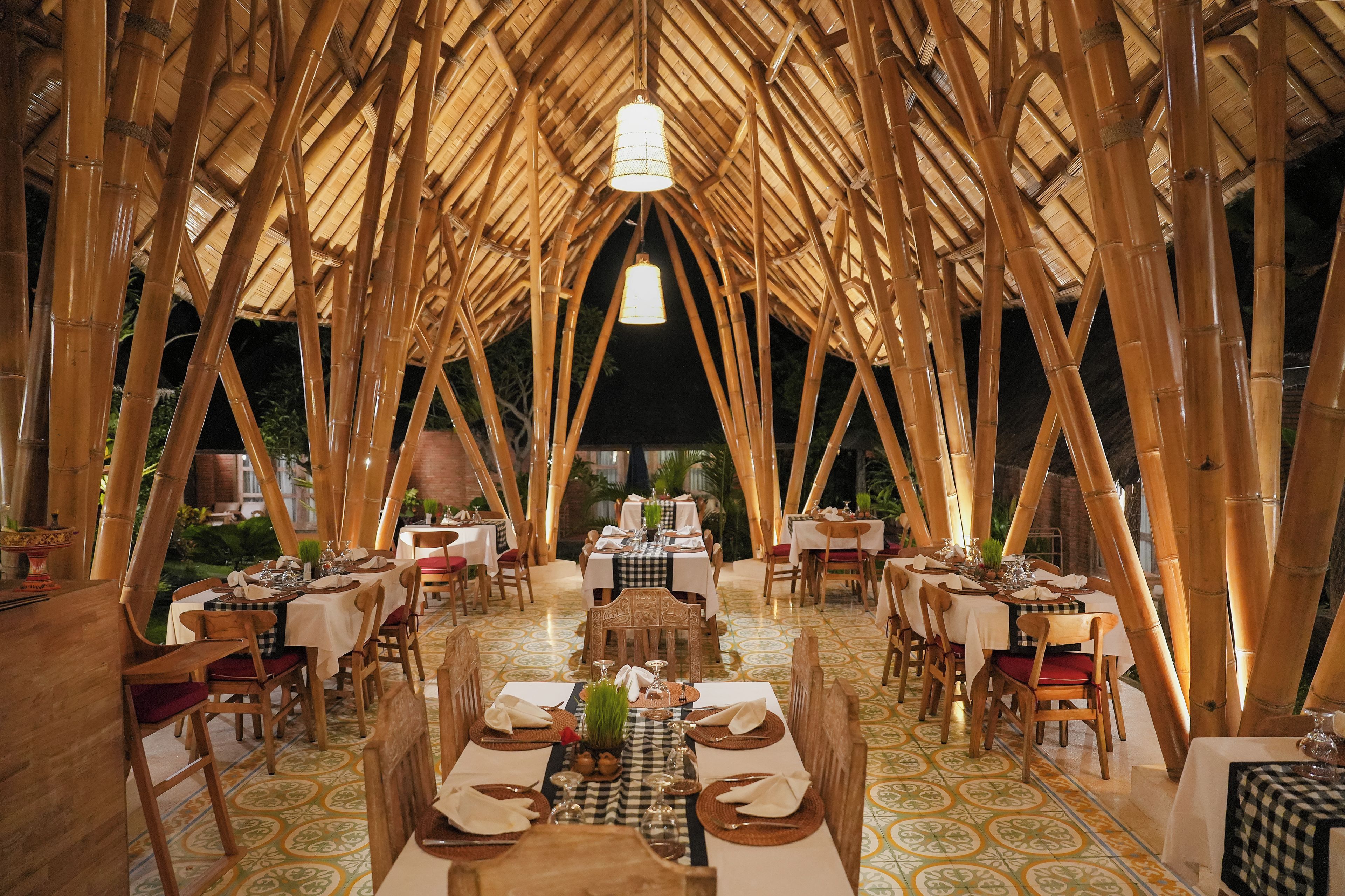 Un comedor interior con estructuras de techo de bambú, mesas dispuestas con manteles blancos y sillas.
