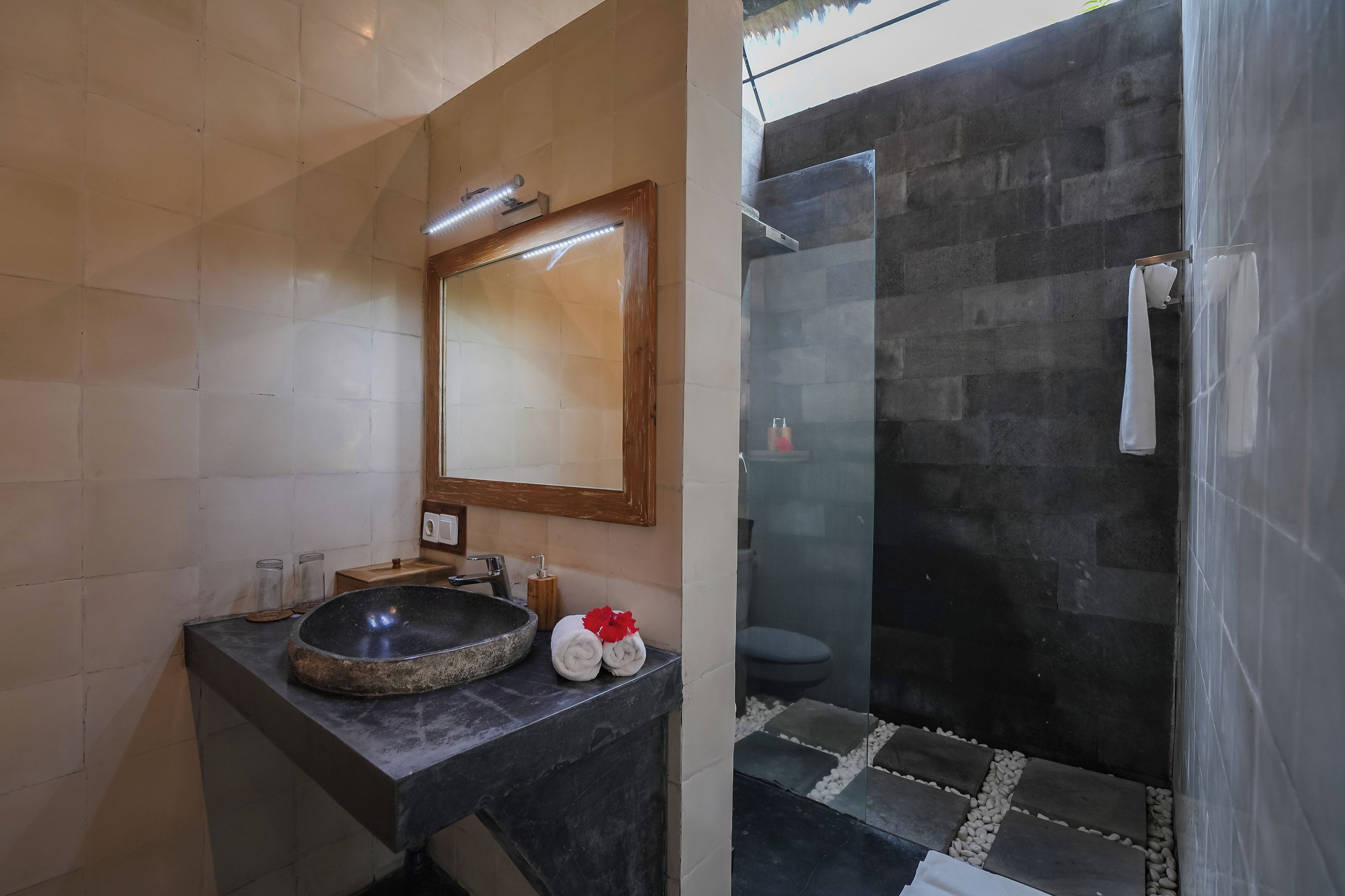 A bathroom with a stone sink, a mirror, and a glass-enclosed shower area.