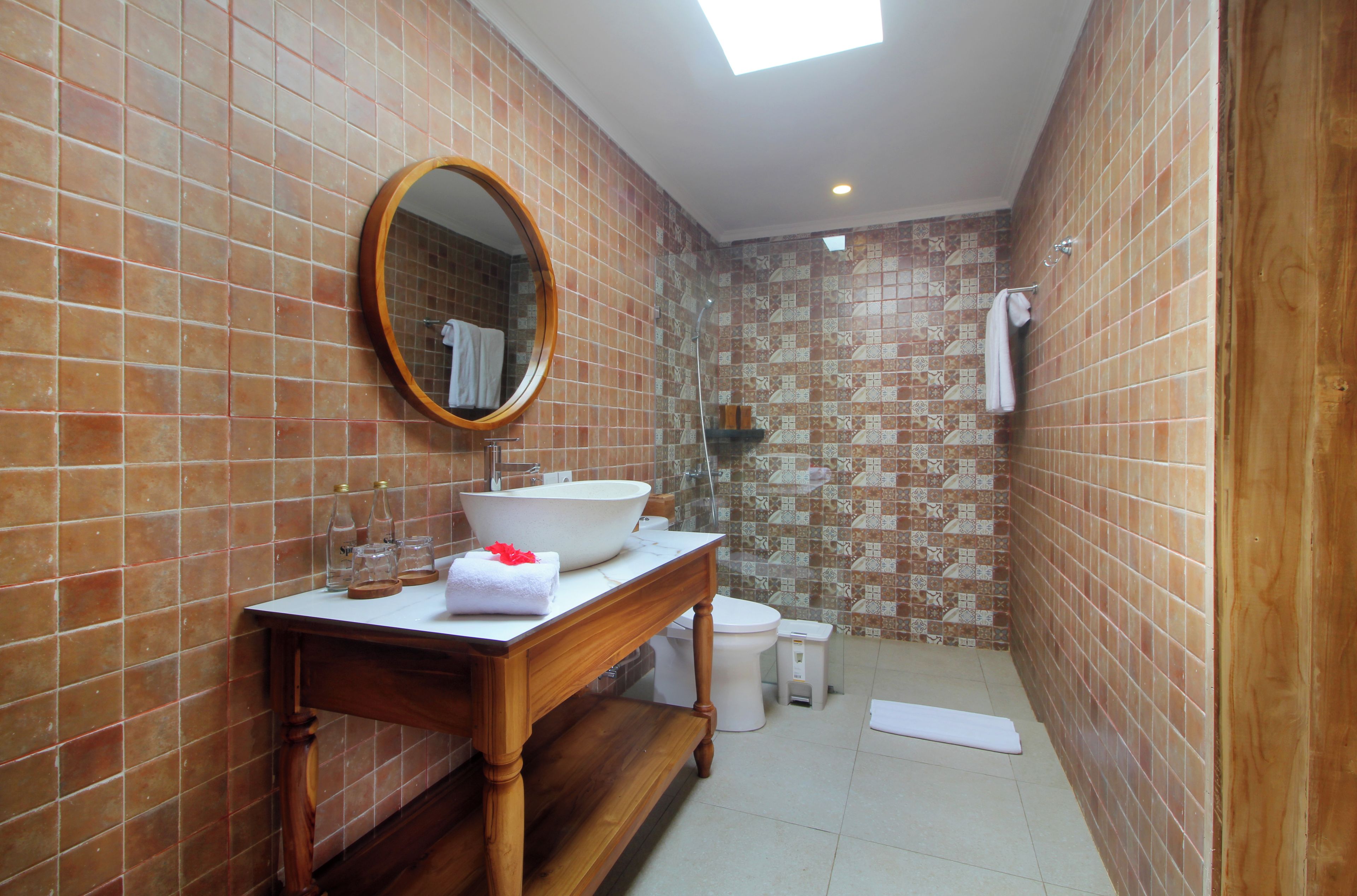 A bathroom with a wooden vanity, a large mirror, a white sink, and a shower area.