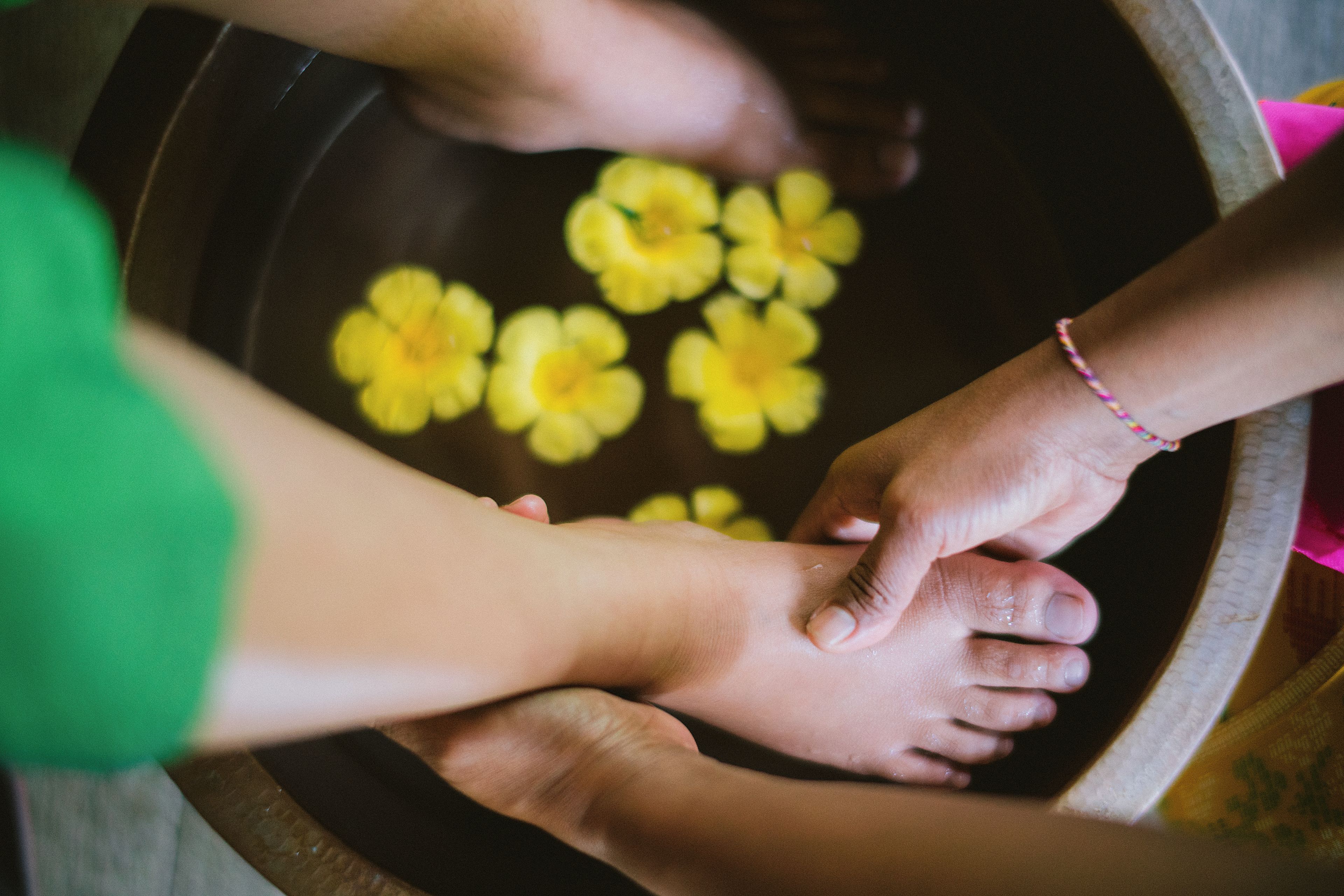 Les mains d’une personne dans un récipient en bois, avec des fleurs jaunes.