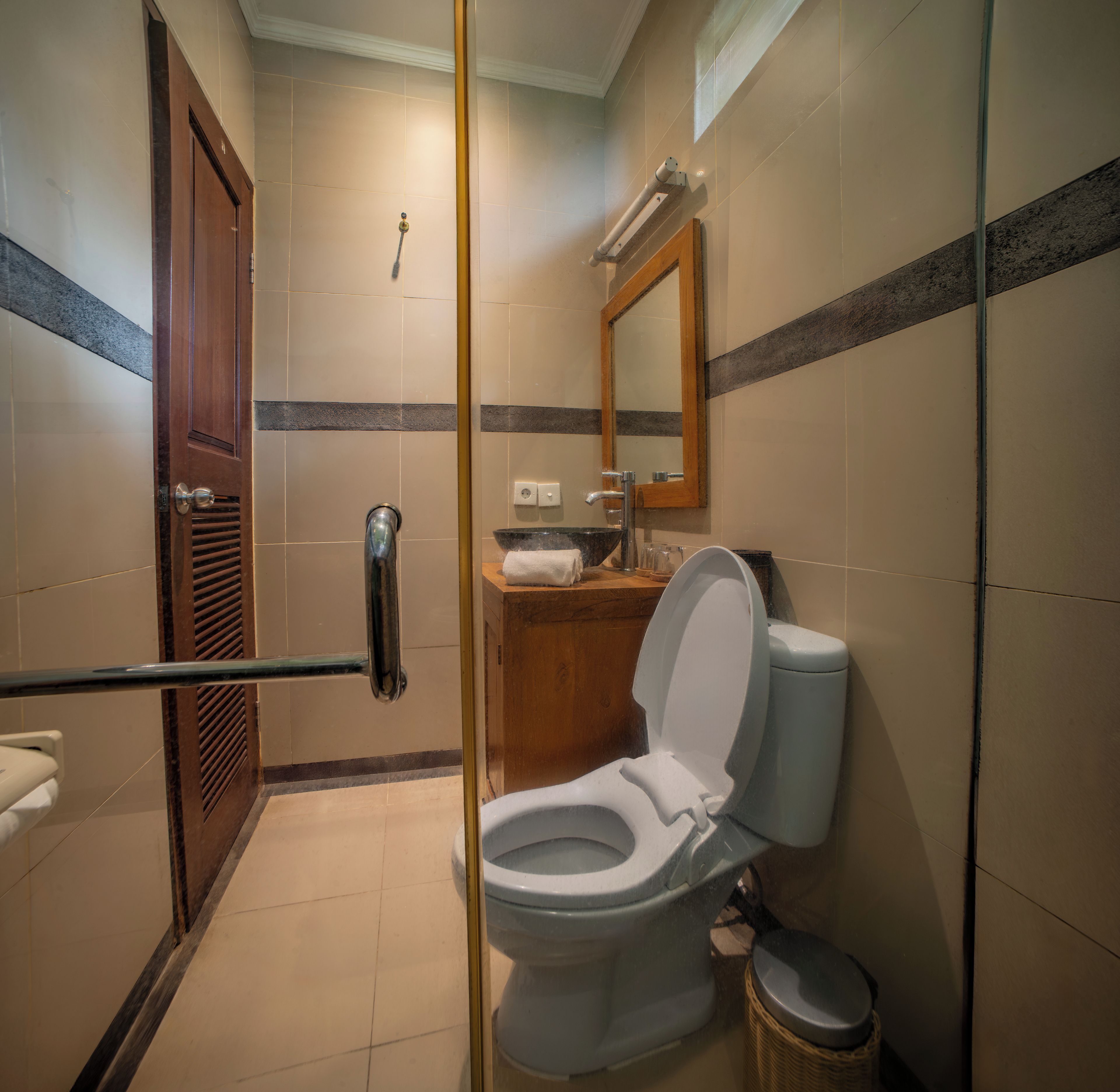 Et badeværelse med toilet, håndvask, spejl og bruseområde.