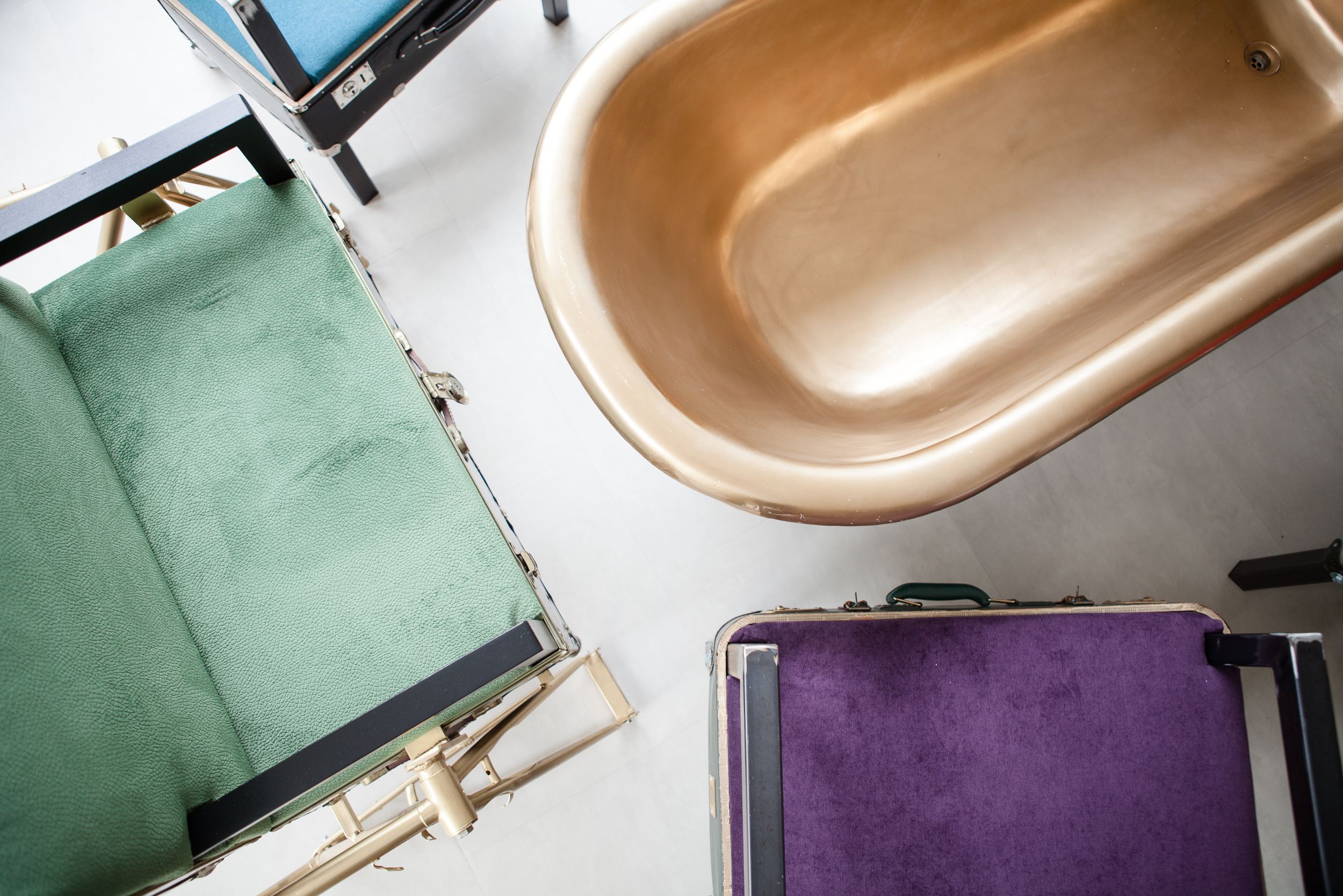 A bathroom with a bathtub, a green chair, and a purple suitcase.