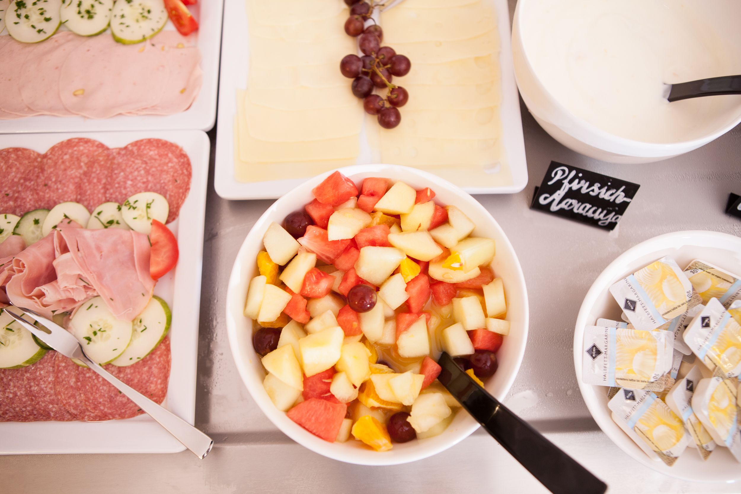 Ein Tisch mit verschiedenen Speisen, darunter Aufschnitt, Käse und eine Schüssel Obstsalat.