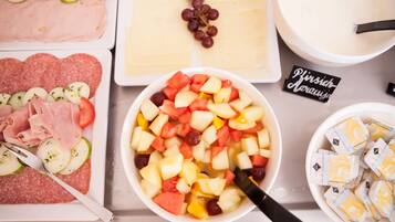 Ein Tisch mit verschiedenen Speisen, darunter Aufschnitt, Käse und eine Schüssel Obstsalat.