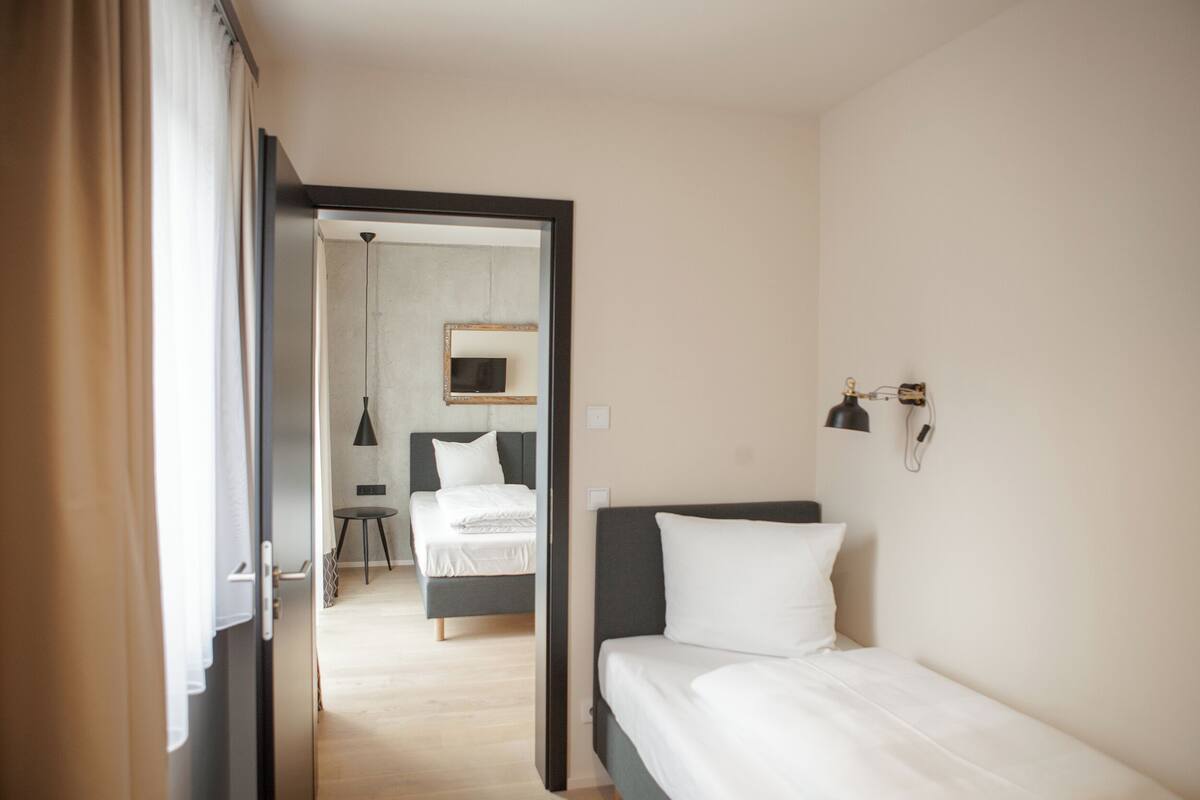 Ett modernt hotellrum med en enkel säng, ett litet bord och en stol.