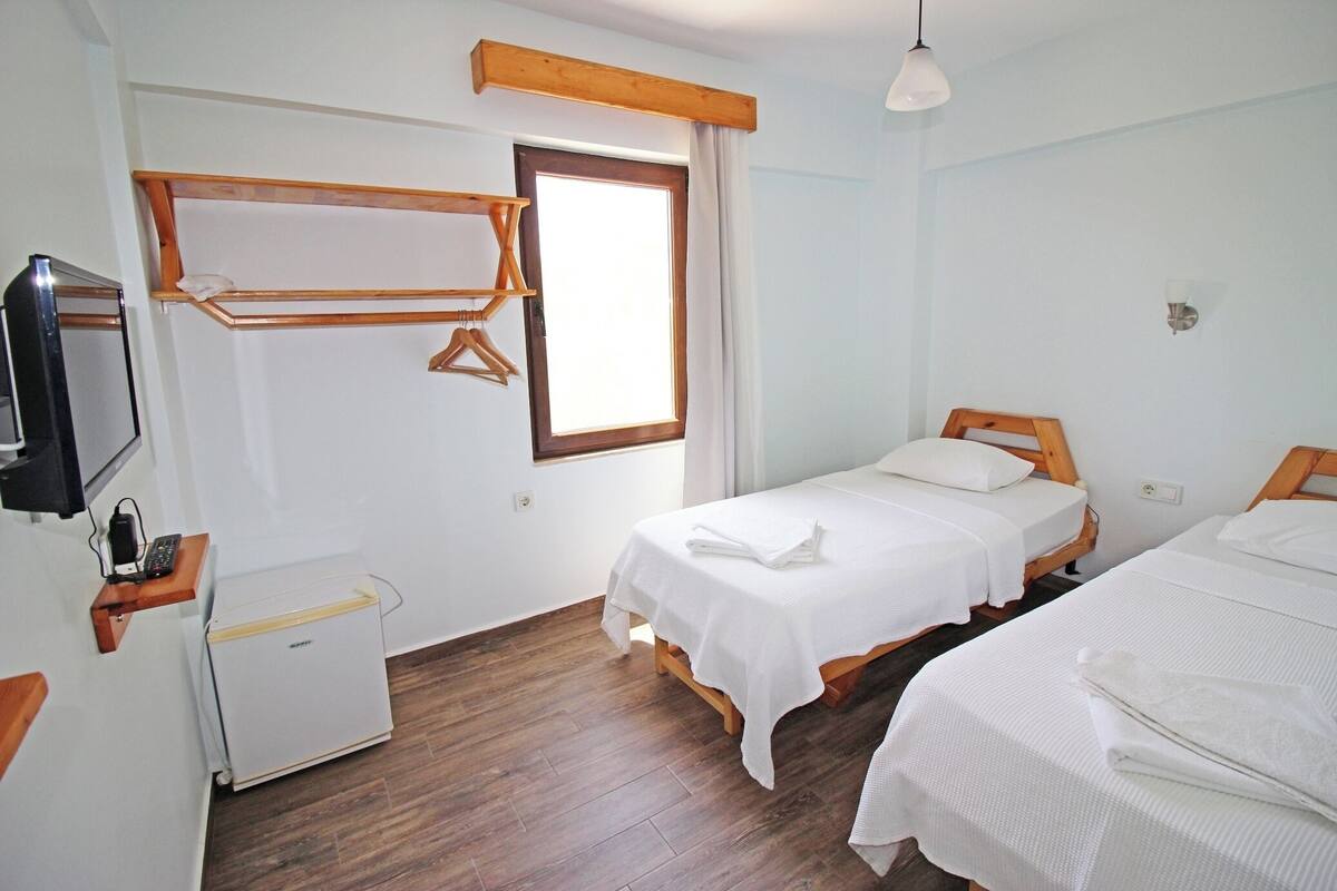 A bedroom with two beds, a small desk with a computer, a TV, and a window with curtains.
