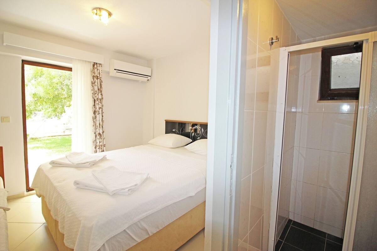 A hotel room with a bed, a shower, and an air conditioning unit.