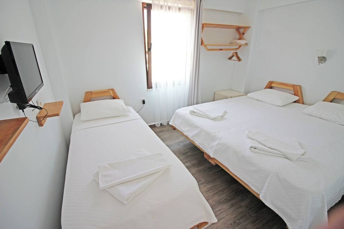 A hotel room with two single beds, a TV, a window with curtains, and a wooden shelf.