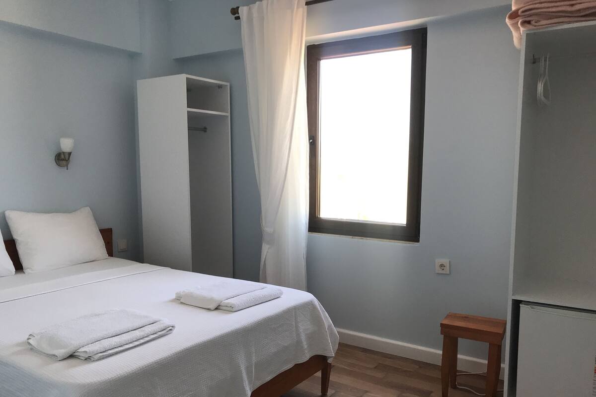 A bedroom with a bed, a wardrobe, a small table, and a window.
