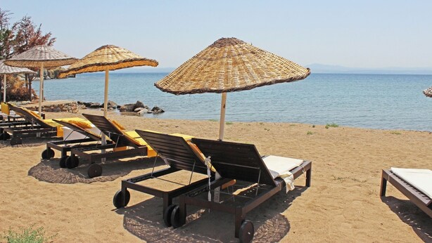 Beach chairs and thatched umbrellas on a sandy beach with a view of the sea. - Arsipel Hotel (Bozcaada)
