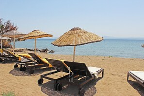 Des chaises de plage et des parasols en chaume sur une plage de sable, avec vue sur la mer.
