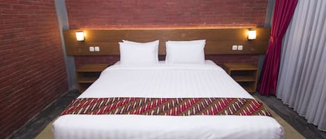 Habitación de hotel con pared de ladrillo, cabecero de madera, cama con sábanas blancas y una manta estampada.