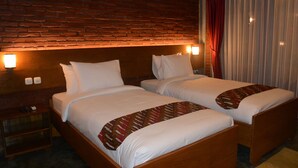 A hotel room with two single beds, a brick wall, a nightstand, and a window with curtains.